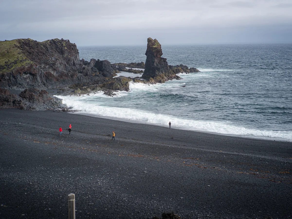 Ein isländischer schwarzer Kiesstrand mit einer Felsnadel im Meer, als Beispiel für Djupalonssandur